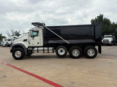Mack GR64F dump truck side view showing black dump body, white cab, chrome wheels, and tag lines on the door and side panels.