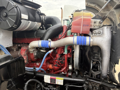 Engine bay of a 2021 Mack GR64F dump truck with blue hose couplings, coolant reservoir, and red engine components visible.