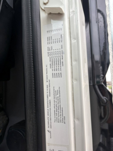 Label on door jamb with vehicle VIN and specifications text for a Mack GR64F dump truck. Visible: long block of small text, numbers arranged in a table, likely VIN and production details.