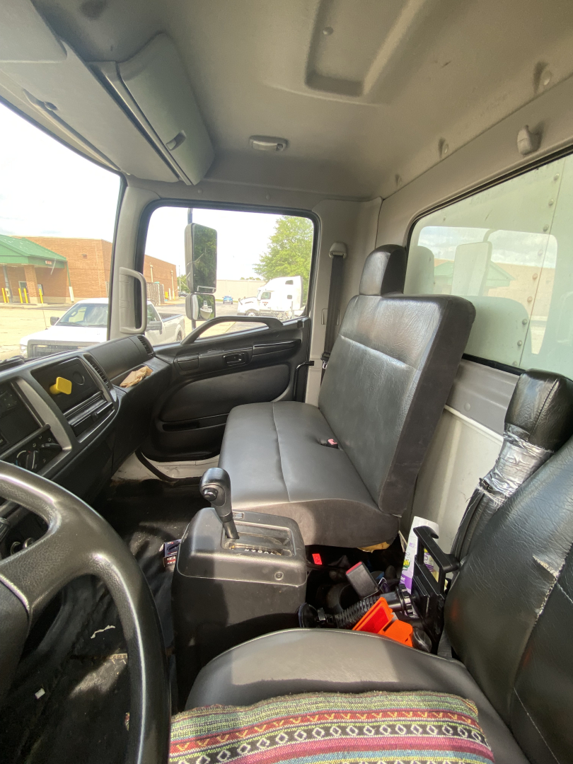 Truck interior cab with steering wheel on left, bench seat, gear shifter, and dashboard; visible panels and windows; no legible labels or numbers.