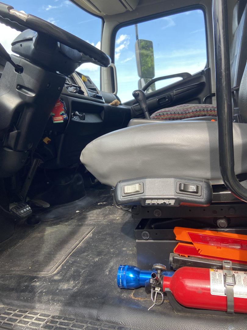 Truck cabin interior with driver's seat and steering wheel, view from floor shows a blue valve fitting and red fire extinguisher near the floor in a Hino conventional truck.