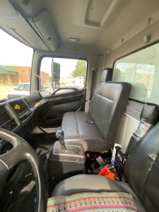 Truck interior cab with steering wheel on left, bench seat, gear shifter, and dashboard; visible panels and windows; no legible labels or numbers.