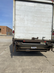 Truck rear view showing cargo box and hydraulic lift gate with license plate area and back doors.