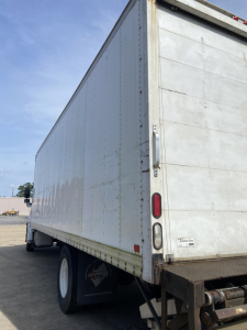 Truck trailer rear and side view showing large white cargo box, rear doors, and dual rear wheels.