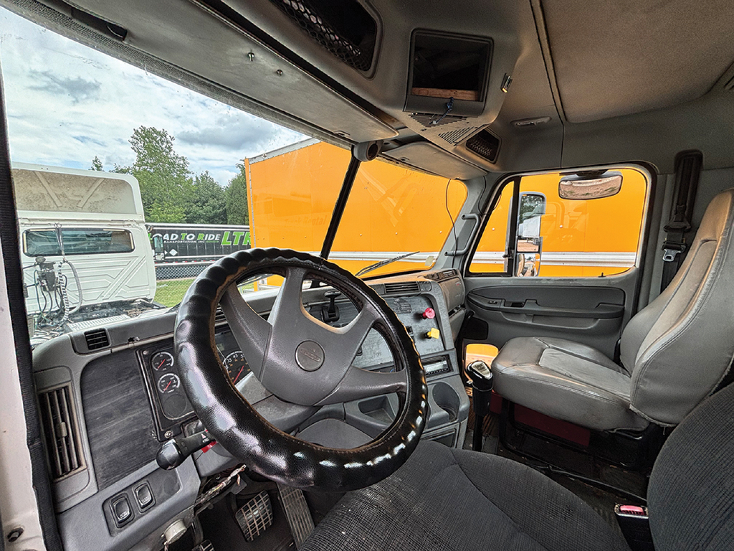 Cab interior of a Freightliner CL120 Columbia showing steering wheel, dashboard controls, and gray seats.
