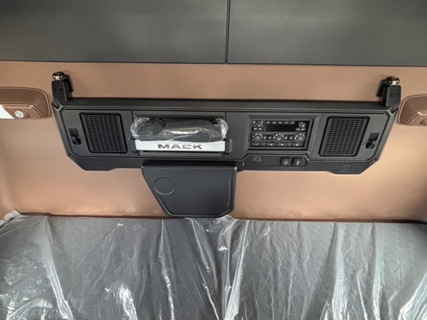 Mack PR64T76H truck dashboard area showing center console with built-in radio, two air vents, and MacK badge; beige interior.