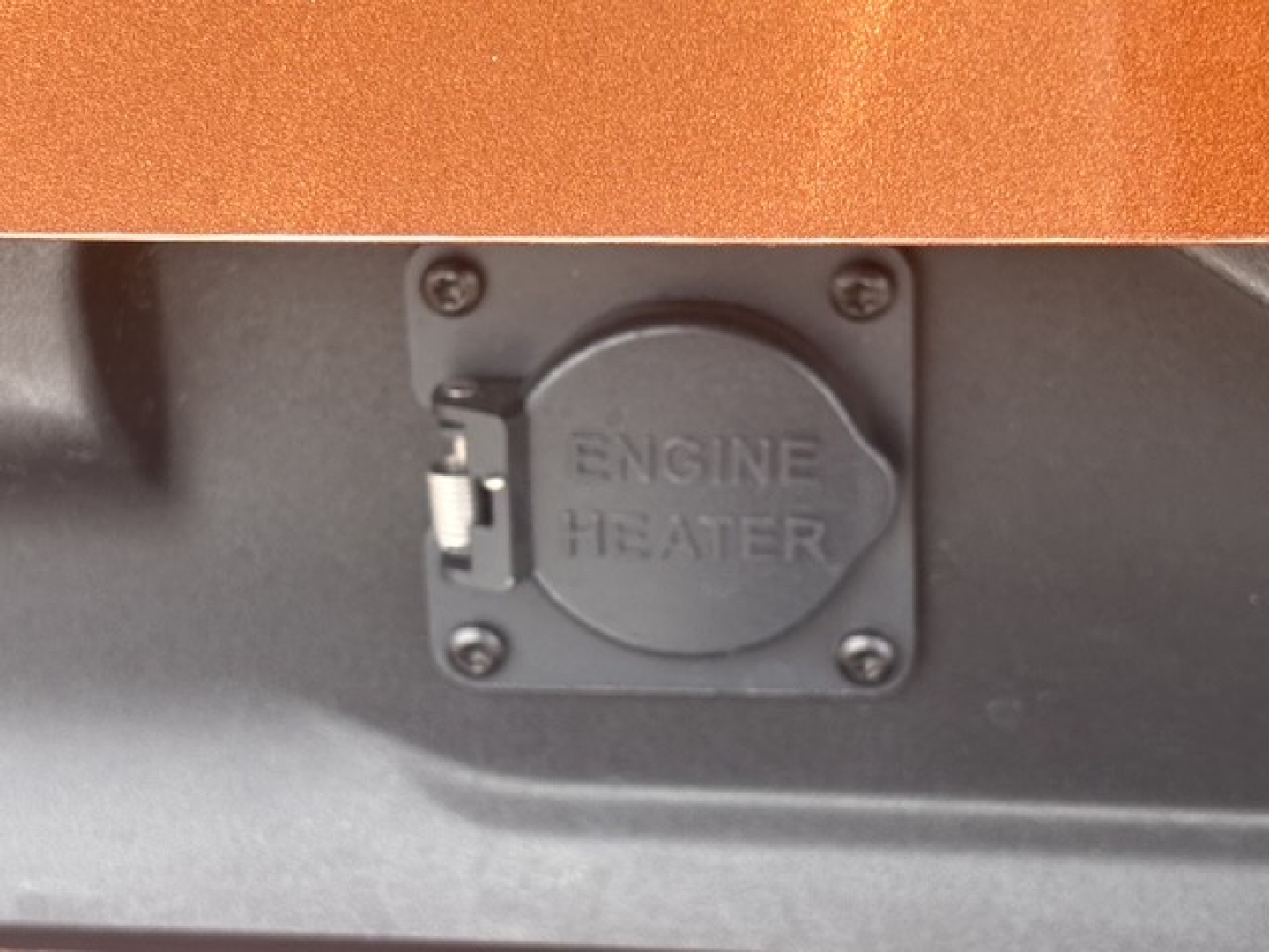 Engine heater access panel with circular cap labeled ENGINE HEATER on a dark surface.