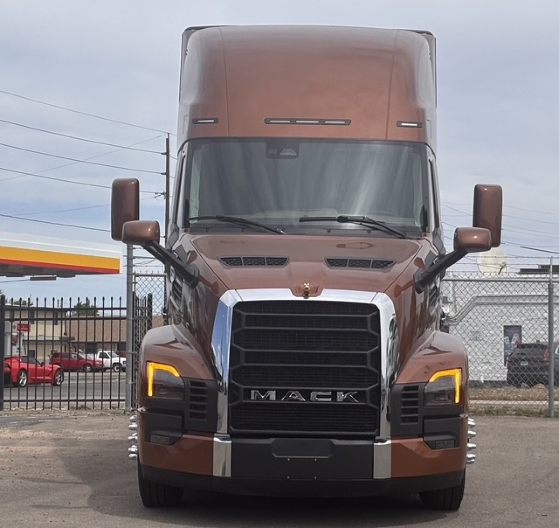 Front view of a brown 2027 Mack PR64T76H conventional sleeper truck showing large grille, LED daytime running lights, and chrome accents.