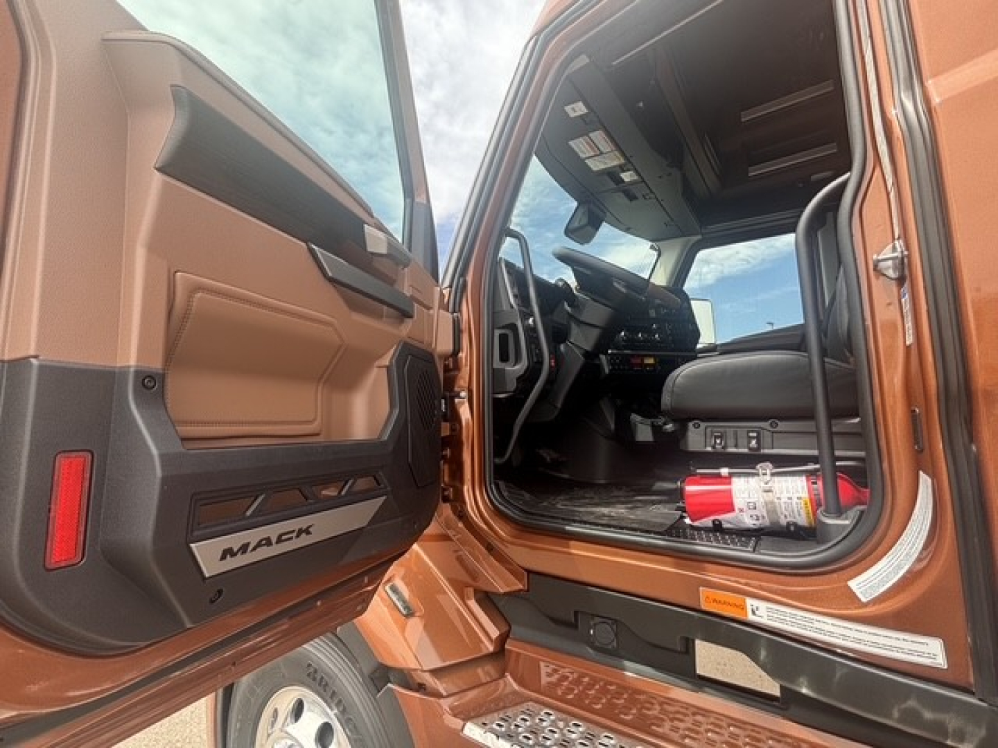 Mack PR64T76H truck interior and open door showing cab, steering wheel, dashboard, and a fire extinguisher in the footwell.