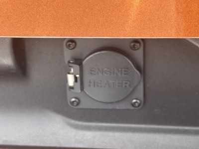 Engine heater access panel with circular cap labeled ENGINE HEATER on a dark surface.