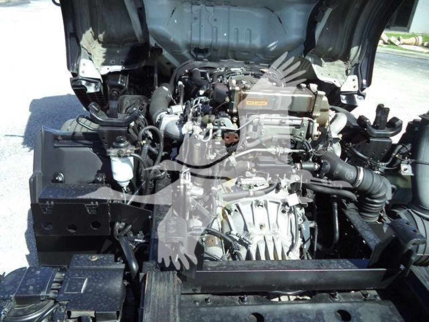 Isuzu NPR XD engine bay view showing engine and surrounding components. Visible text on engine includes 'D-MAX' style markings; no legible resistor or fluid labels clearly readable.