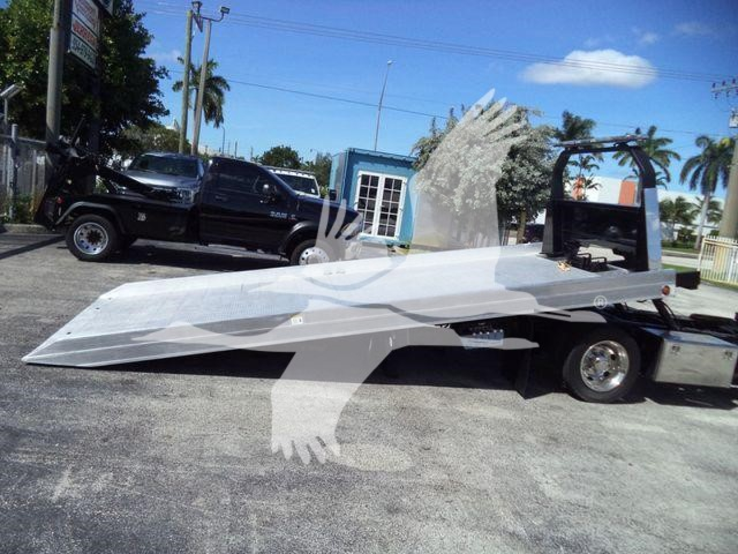 Isuzu NPR XD rollback truck with a flatbed and crane hitch viewed from the side.