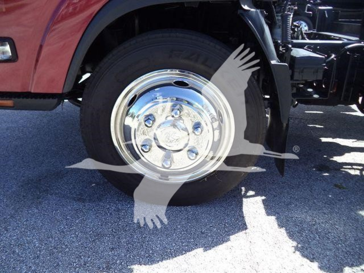 Isuzu NPR XD rollback truck front wheel and chrome hubcap visible; partial engine area and tow equipment mounting in background.