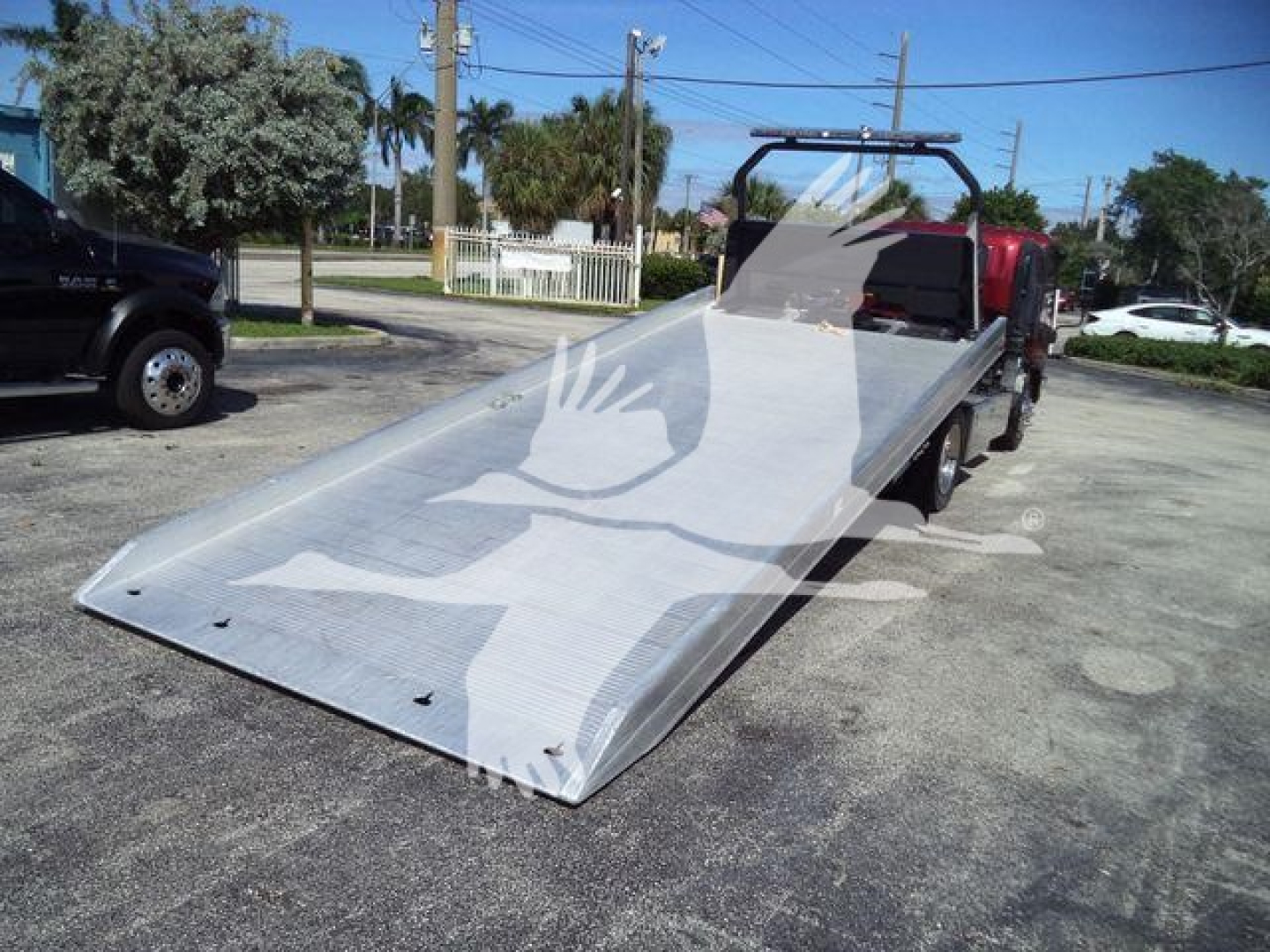 Isuzu NPR XD rollback truck with extended flatbed ramp in service truck yard.
