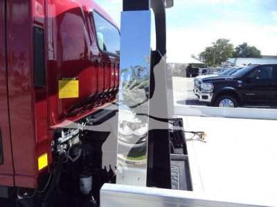 Isuzu NPR XD rollback truck side view showing a chrome vertical post with hydraulic components and a red cab in the background.
