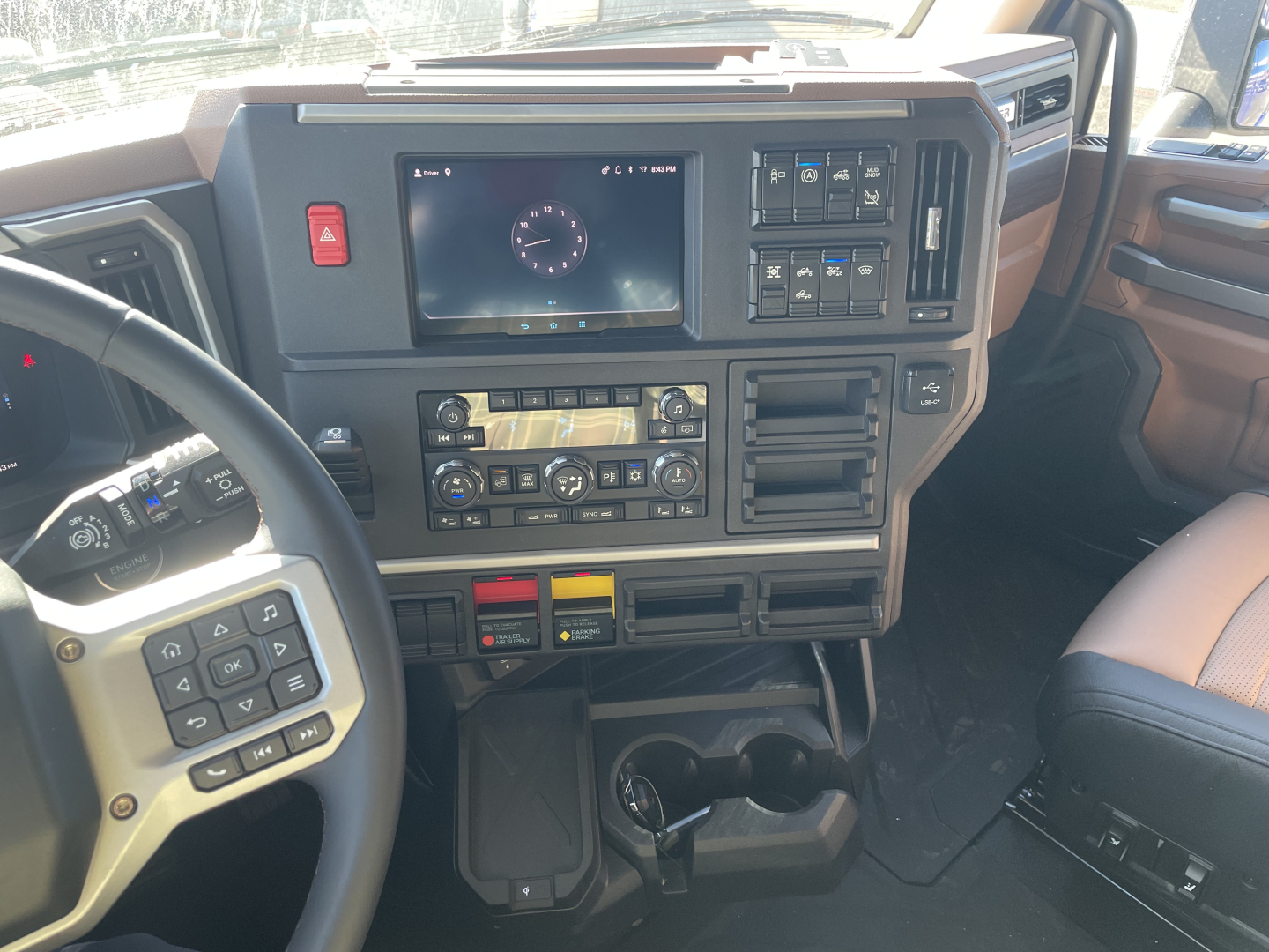 Cab interior of a 2026 Mack PR64T76H truck showing steering wheel, dashboard with digital screen, center console, climate controls, and gear selector; view is from driver’s seat.