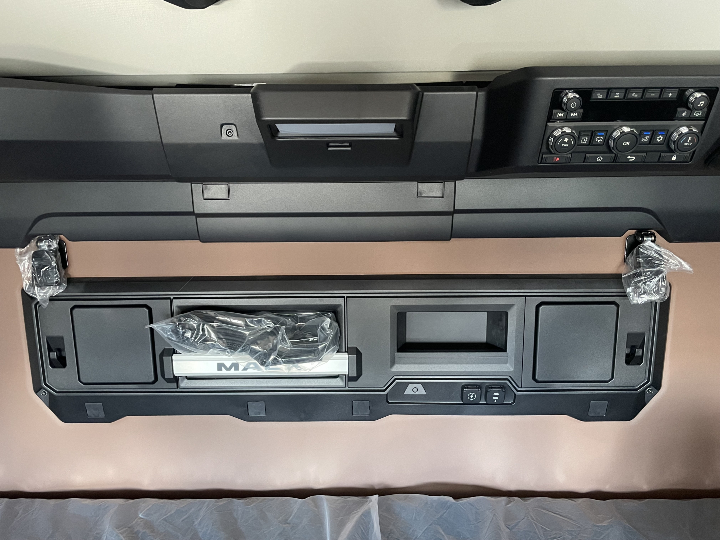 Front interior dash area of a new 2026 Mack PR64T76H truck showing instrument panel, storage compartments, and control console.