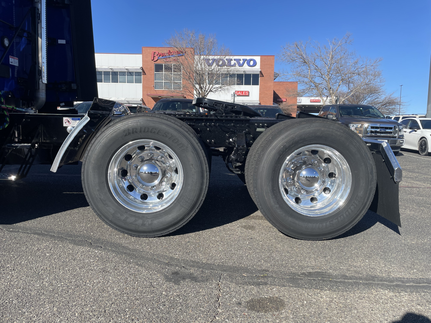 Mack PR64T76H tractor tandem axle drivetrain with dual rear wheels and chrome wheels in a dealership lot.