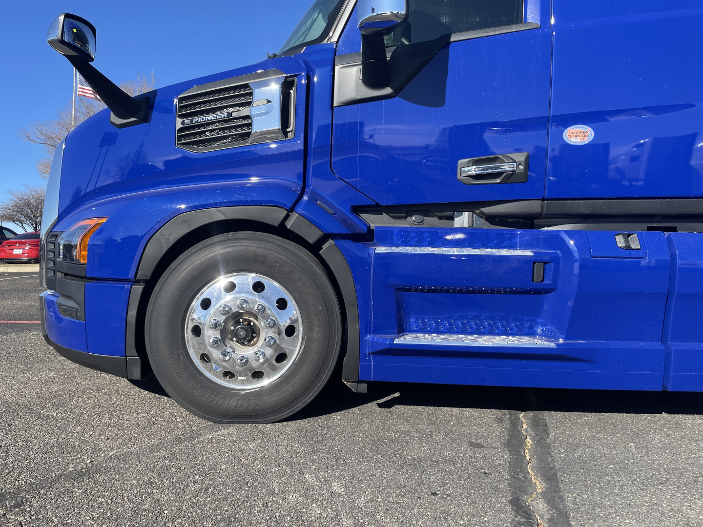 Front left side of a blue Mack PR64T76H truck showing front wheel, fender, and door area with chrome mirror and step. No text visible on the image besides general vehicle details.