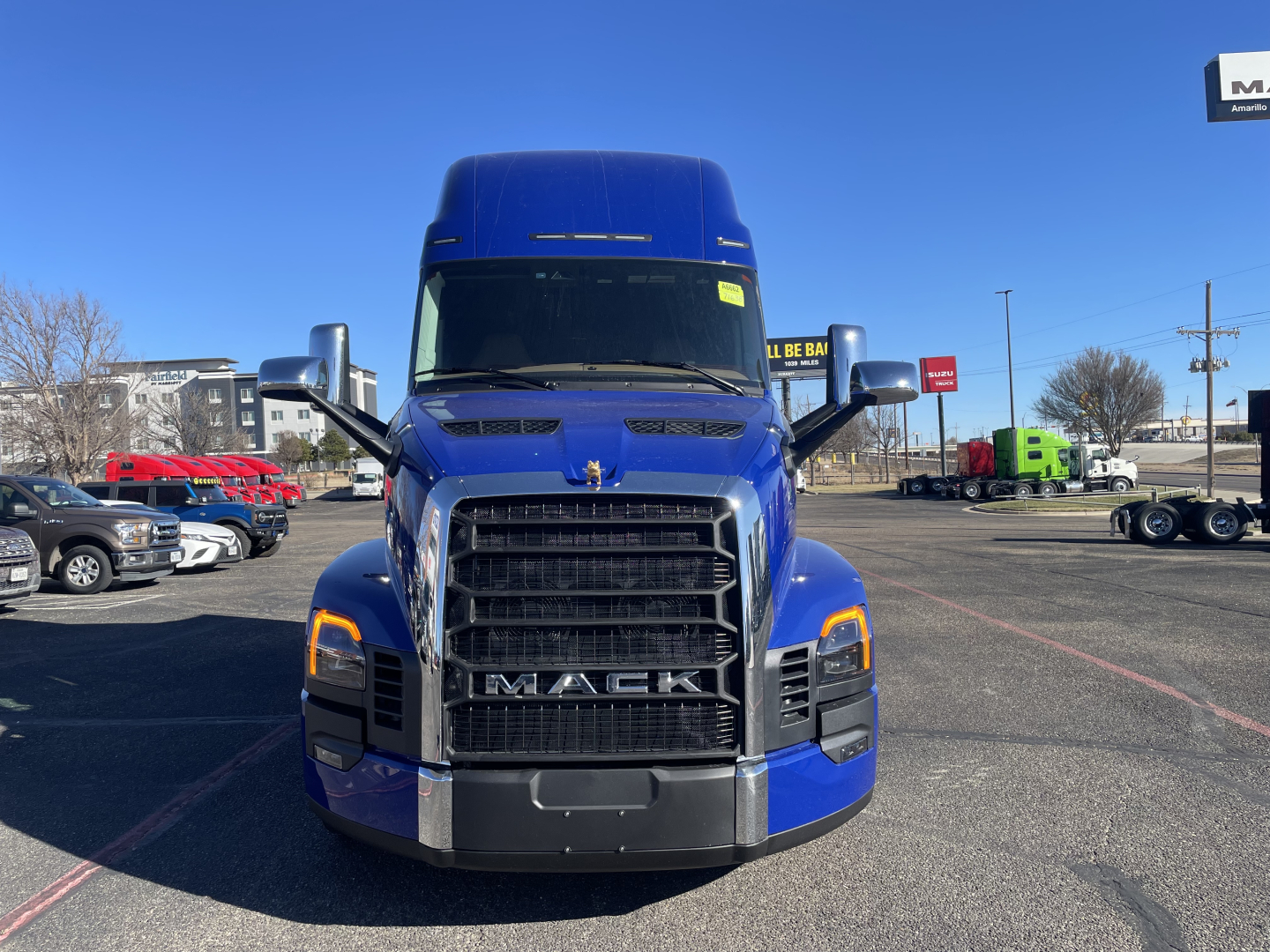 Front view of a blue Mack PR64T76H truck in a dealership lot showing the grille with MACK badge and headlight assemblies.