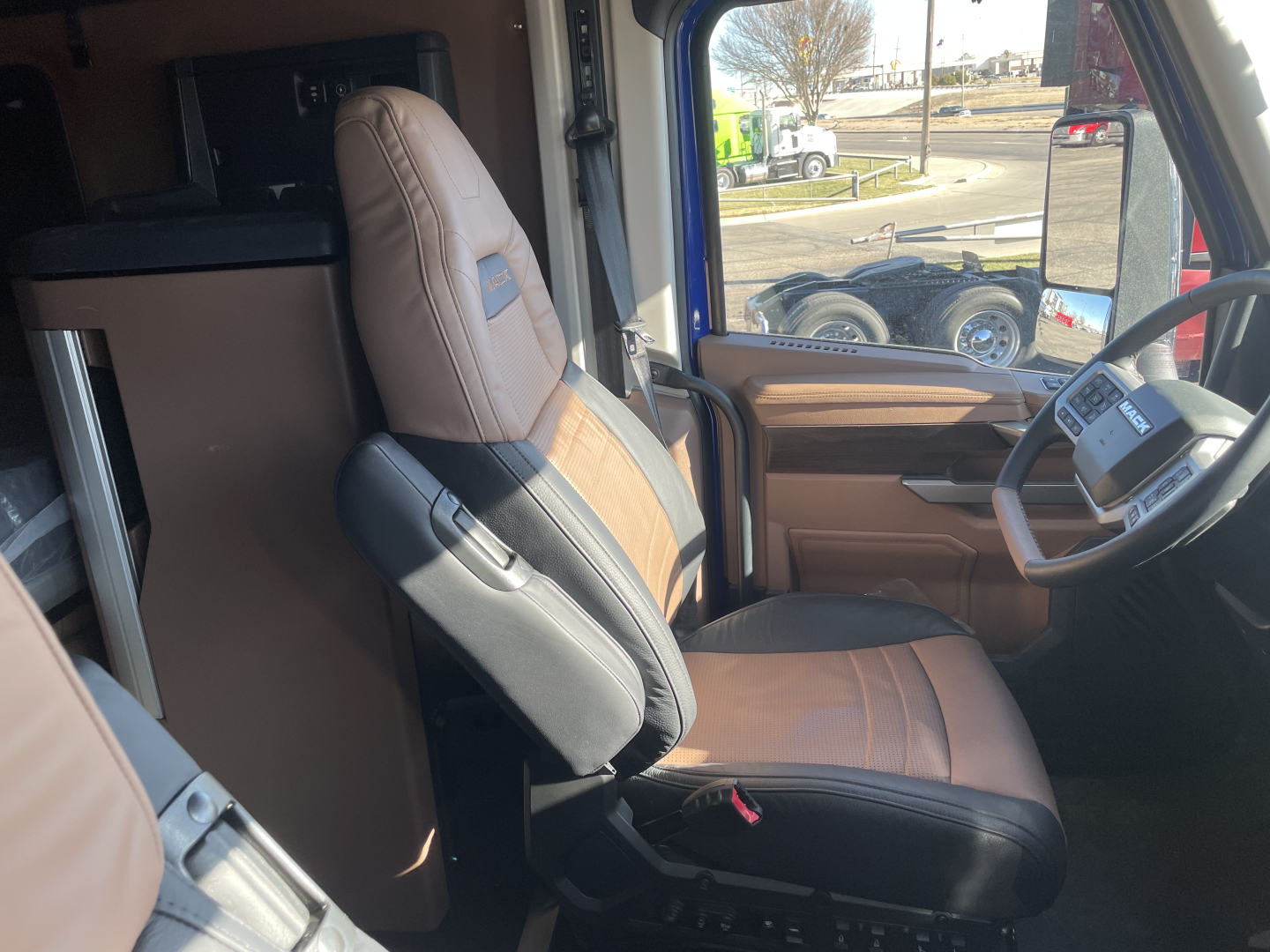 Truck cab interior showing driver seat and passenger seat in tan and black, with steering wheel and dashboard visible.