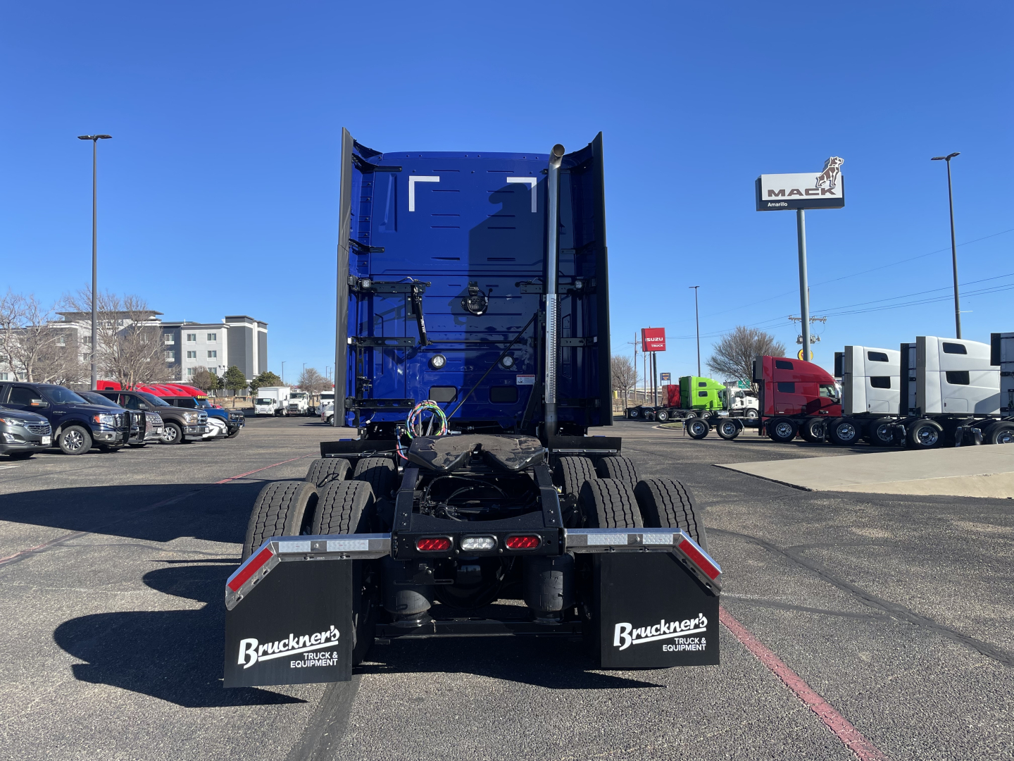 Truck chassis rear view showing fifth wheel and mud flaps with Buckner Equipment branding. Open dual rear tires and blue cab in distance.