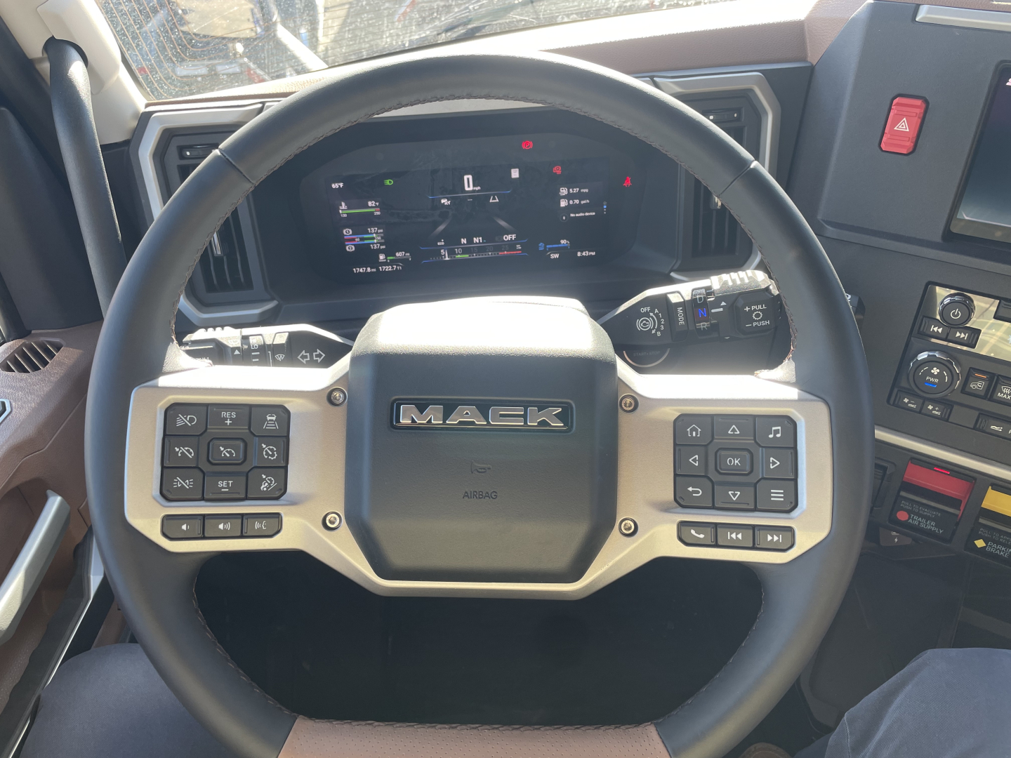 Steering wheel of a Mack PR64T76H truck showing mounted controls and digital dash display in the cockpit.