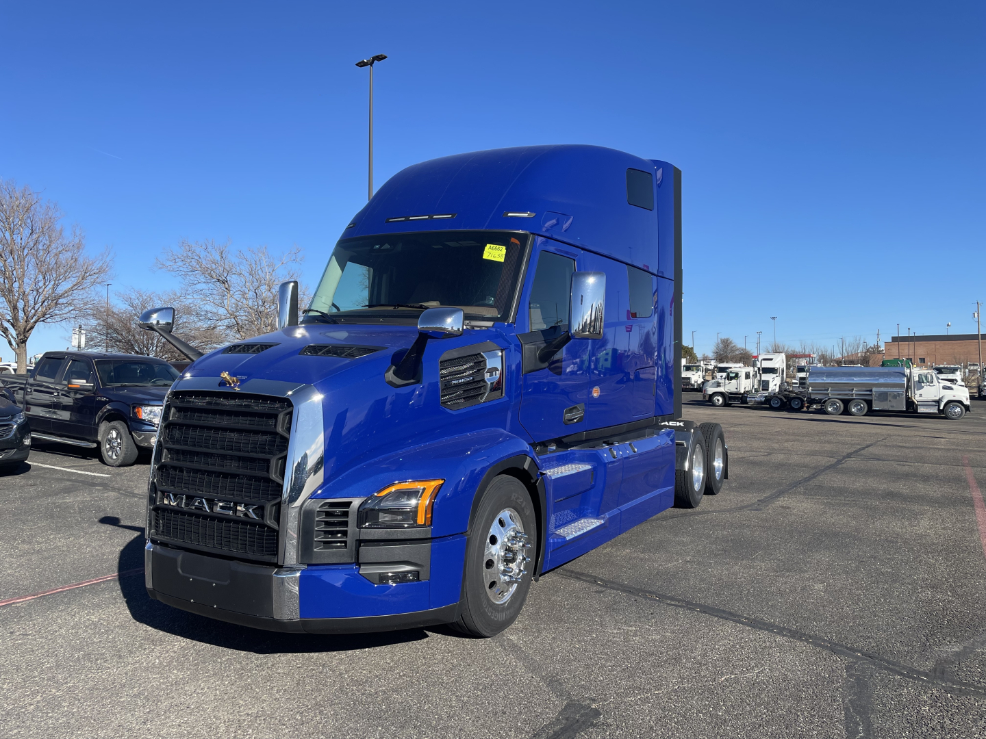 Truck engine bay not visible; exterior side view of a blue Mack PR64T76H sleeper tractor in a dealership lot.