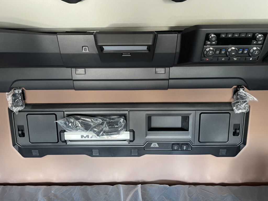 Front interior dash area of a new 2026 Mack PR64T76H truck showing instrument panel, storage compartments, and control console.