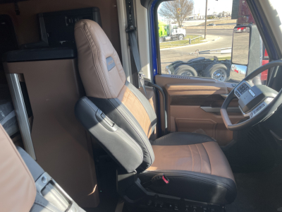 Truck cab interior showing driver seat and passenger seat in tan and black, with steering wheel and dashboard visible.