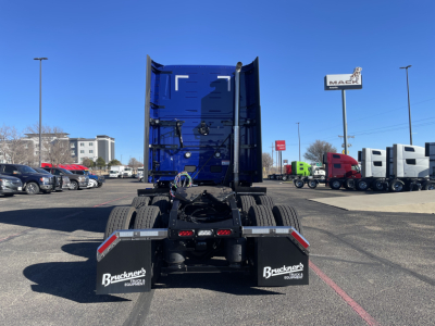 Truck chassis rear view showing fifth wheel and mud flaps with Buckner Equipment branding. Open dual rear tires and blue cab in distance.