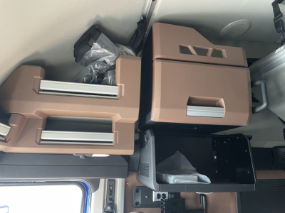 Interior storage compartments and a drawer in a Mack PR64T76H truck cab showing tan plastic storage boxes and a small black tray.