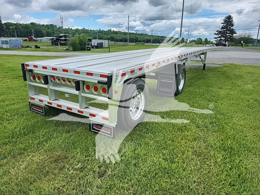 Flatbed trailer in an outdoor setting showing rear and left-side with multiple round taillights, reflective tape, and dual wheels; model tag and TR065705 visible.