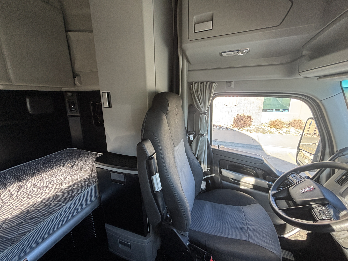 Cab interior of a 2022 Kenworth T680 showing driver's seat and sleeper bunk area with overview of cabin fixtures.