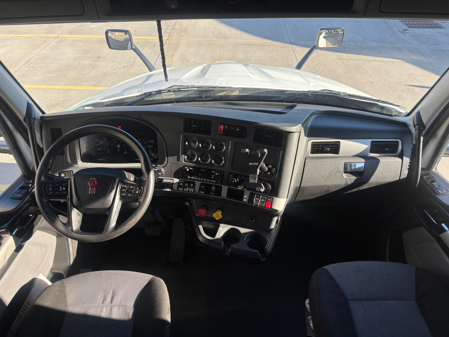 Kenworth T680 cab interior dashboard and steering wheel view from driver's seat, with gauges, controls, and mirrors visible.