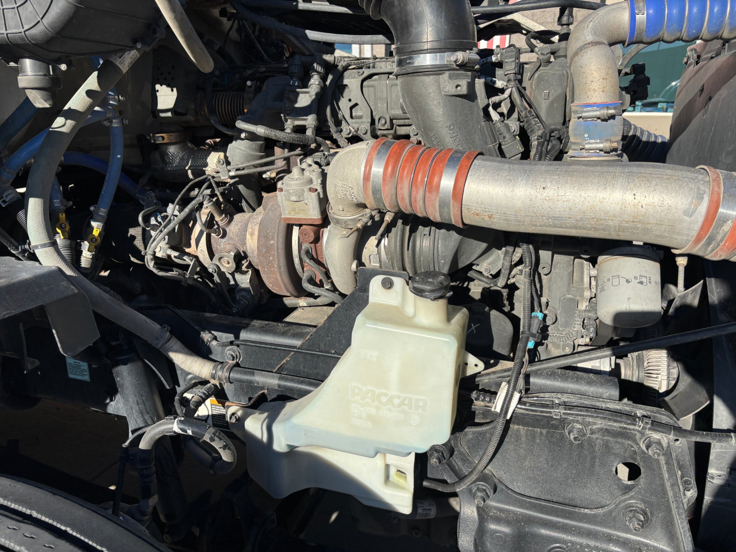 Kenworth T680 engine bay showing coolant reservoir and turbocharger with rubber hoses and metal piping.