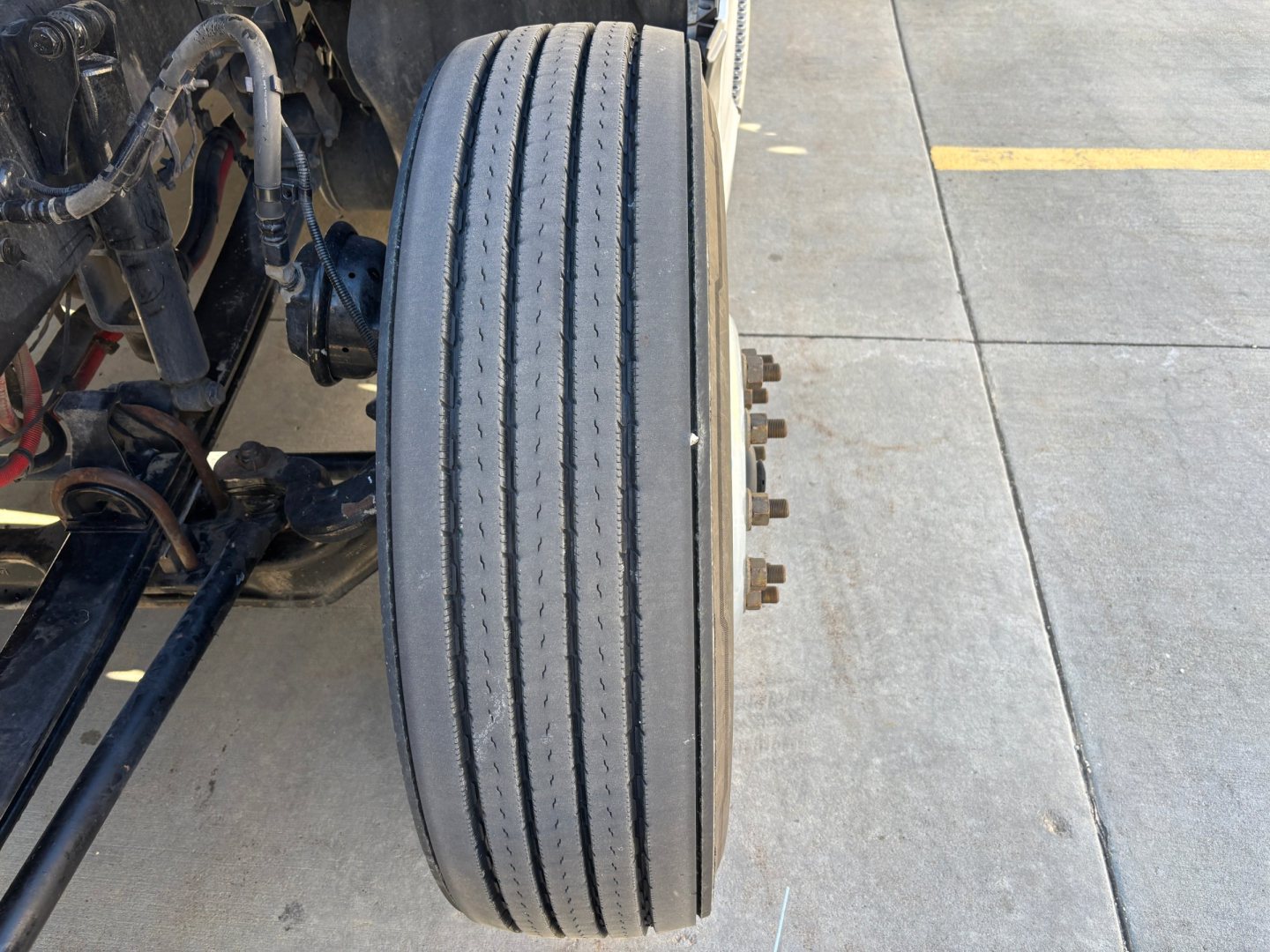Kenworth T680 front wheel and suspension components visible with triple-tire tread line and axle bolts.