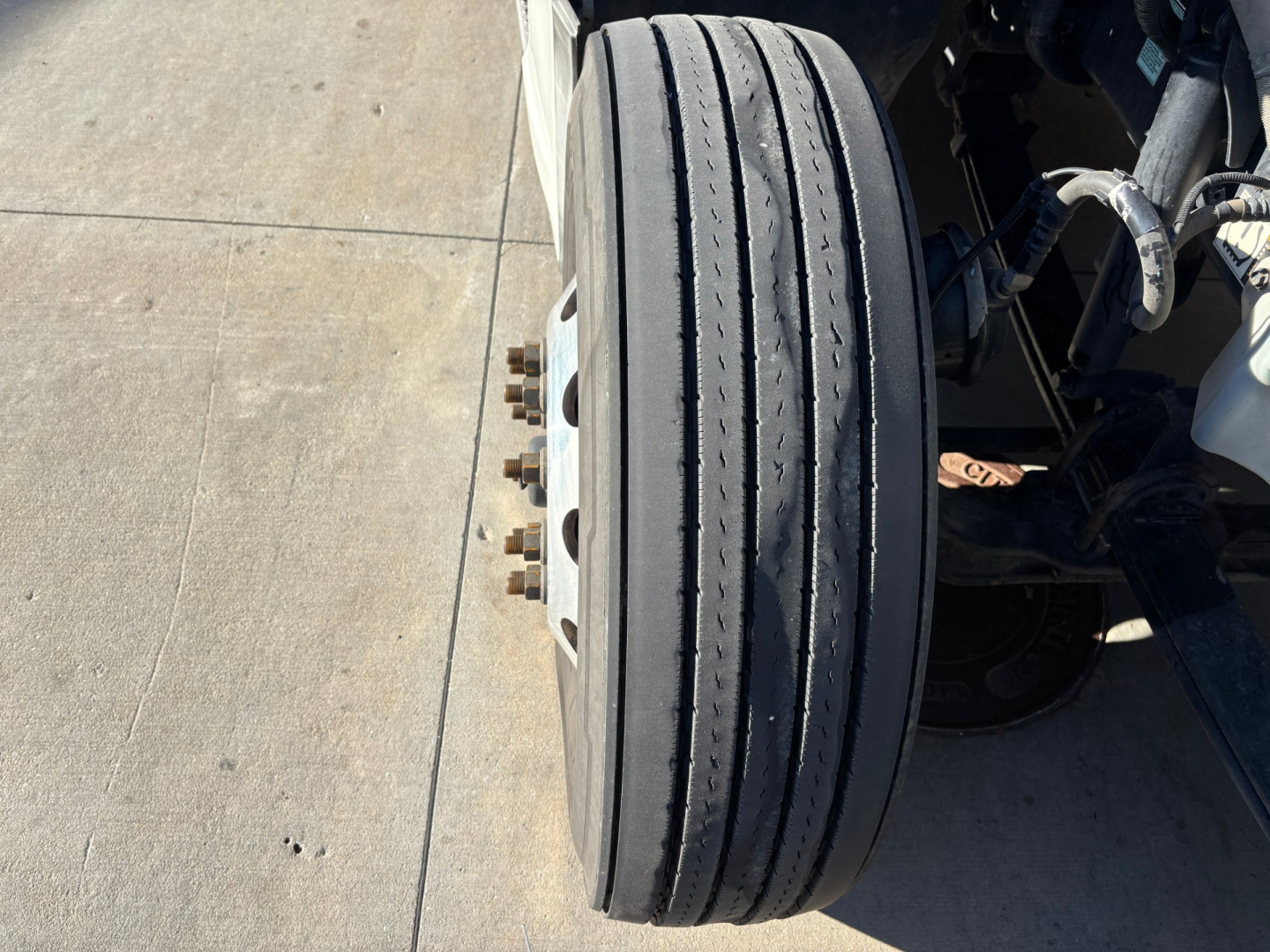 Dual-steelband Kenworth T680 front steer tires and wheel assembly showing axle and suspension components.