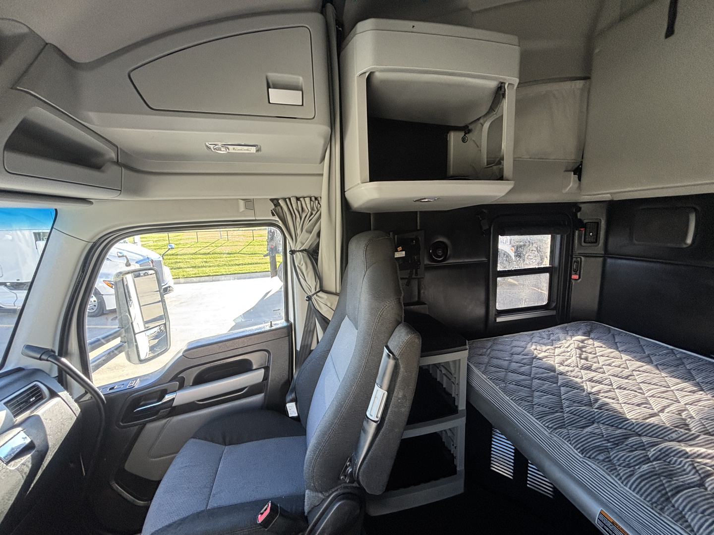 Kenworth sleeper cab interior view with bunk bed, overhead cabinet, and dashboard area. Text visible on panels but not highly legible.