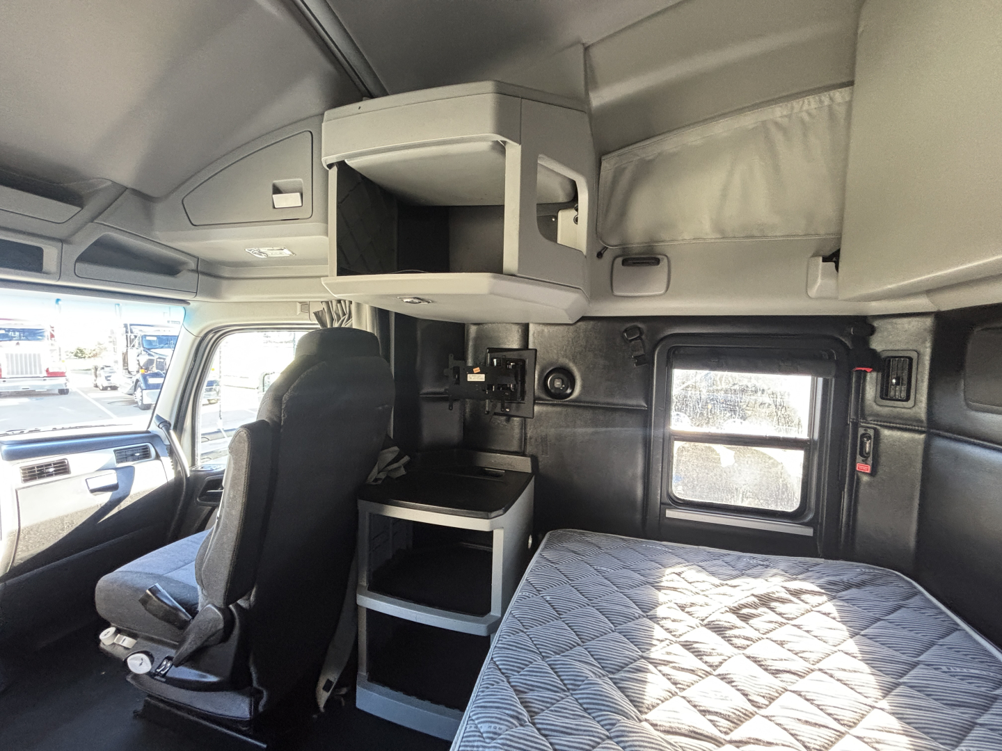 Kenworth T680 sleeper cab interior showing overhead storage, bunk area, and driver seat with window and dashboard visible.