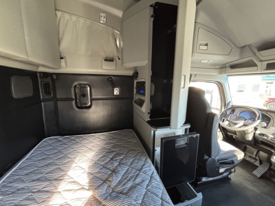 Cab interior of a Kenworth truck showing a bed area with quilted mattress, side panels, and a driver cockpit; no visible equipment labels or fluid text captured.