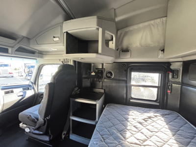 Kenworth T680 sleeper cab interior showing overhead storage, bunk area, and driver seat with window and dashboard visible.