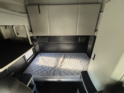 Truck cab sleep area with quilted mattress and overhead storage in a Kenworth T680 sleeper berth interior.