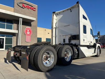 Kenworth T680 tractor rear and sleeper cab with white exterior, dual rear axles, chrome wheels, and fifth wheel; dealership building in background.