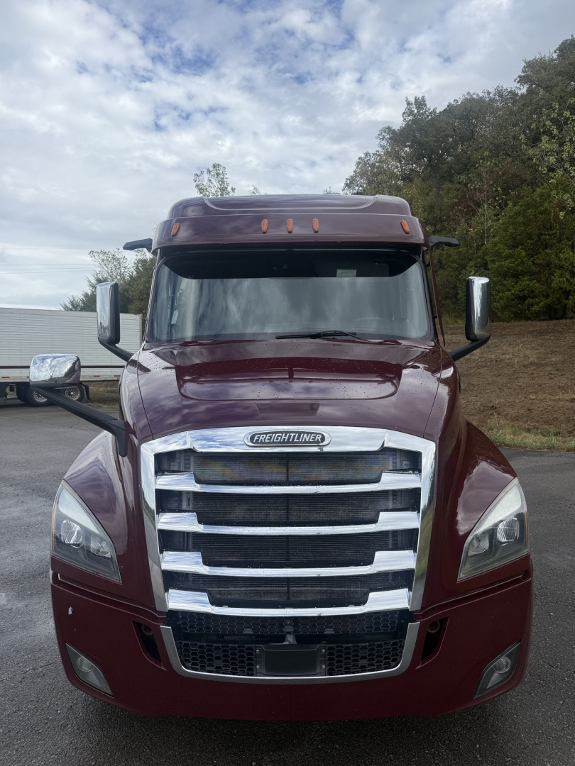 Truck front view of a maroon 2021 Freightliner Cascadia 126 with large chrome grille, headlights, mirrors, and sleeper cab. VIN and stock info not visible on image.