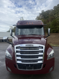 Truck front view of a maroon 2021 Freightliner Cascadia 126 with large chrome grille, headlights, mirrors, and sleeper cab. VIN and stock info not visible on image.