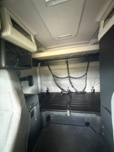 Truck sleeper cab interior showing cargo area with storage net and bed platform in a Freightliner Cascadia 126.