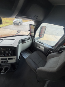 Freightliner Cascadia126 truck cab interior showing dashboard controls, driver seat, and side mirror with a view through windshield.