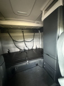 Cab interior of a Freightliner Cascadia sleeper showing a top bunk area with cargo net and storage shelves.