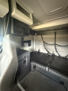 Interior sleeper cab cargo area of a Freightliner Cascadia 126 showing lower storage area, binders, and side ladder rail with netted pocket.